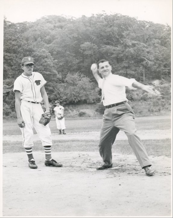 Adult pitching a ball.  Youth pitcher watching.  In the 1950’s.